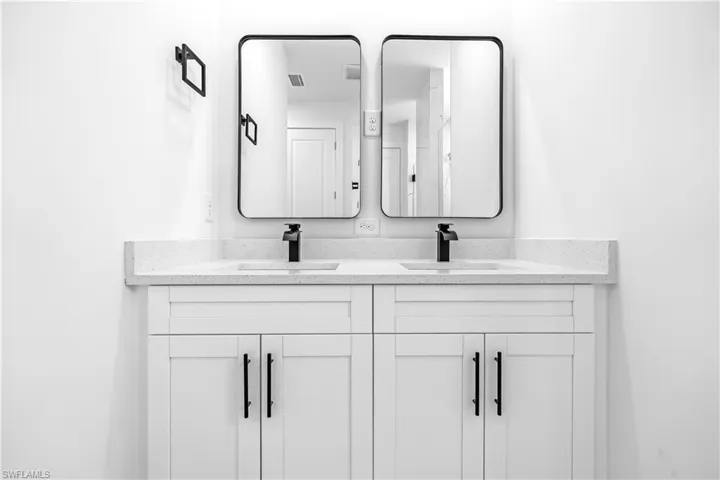 Double vanity featuring white shaker cabinetry, an integrated white countertop with speckle detailing, two undermount sinks, and matte black waterfall faucets