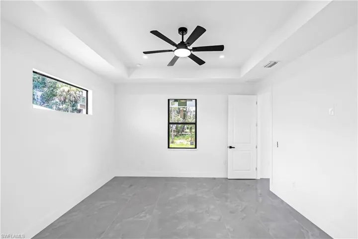 Spacious room featuring modern gray tile flooring, a contemporary black ceiling fan with integrated lighting, and a tray ceiling