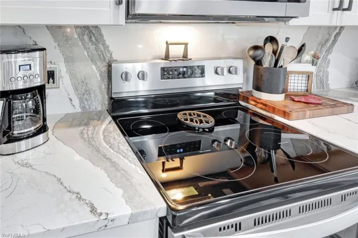 Kitchen with stainless steel appliances, light stone countertops, and white cabinetry