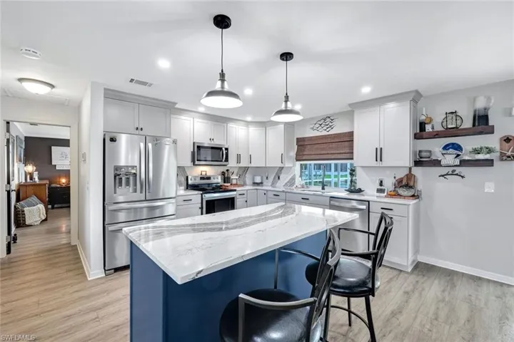 Kitchen featuring appliances with stainless steel finishes, pendant lighting, light stone countertops, a breakfast bar, and light wood-style vinyl flooring