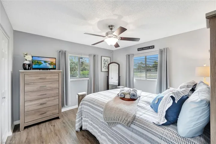 Bedroom with a textured ceiling, light wood-style vinyl flooring, multiple windows, and ceiling fan