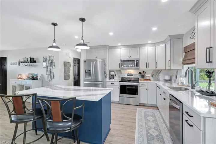 Kitchen with light wood-style vinyl floors, stainless steel appliances, sink, a kitchen island, and pendant lighting
