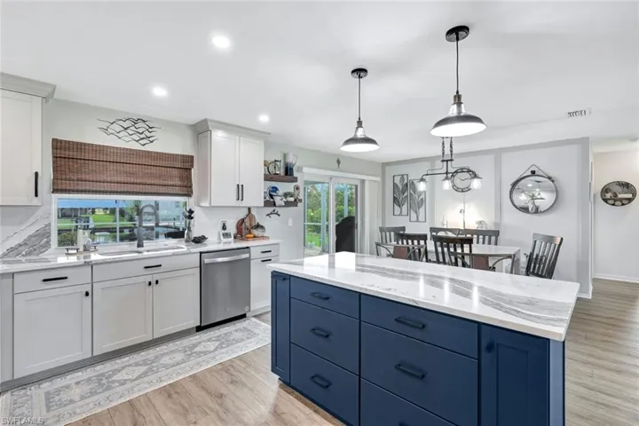 Kitchen featuring a center island, dishwasher, white cabinets, sink, and light wood-style vinyl flooring