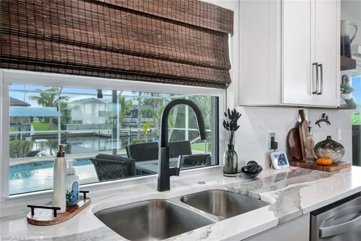 Kitchen featuring stainless steel dishwasher, sink, light stone countertops, and white cabinets