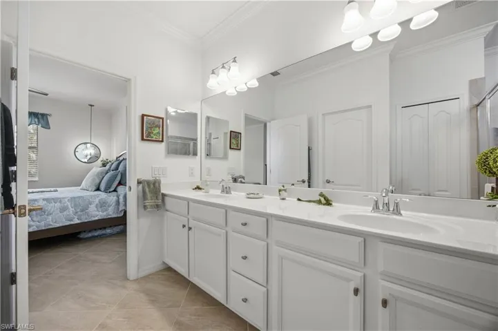 Dual vanity with white cabinetry and integrated sinks, a wide wall-mounted mirror, and tile flooring