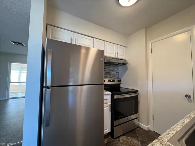 Kitchen featuring white cabinetry, stainless steel appliances, backsplash, and vinyl flooring