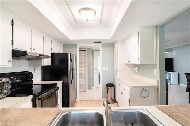 Kitchen featuring crown molding, a tray ceiling, white cabinets, black / electric stove, and light tile floors