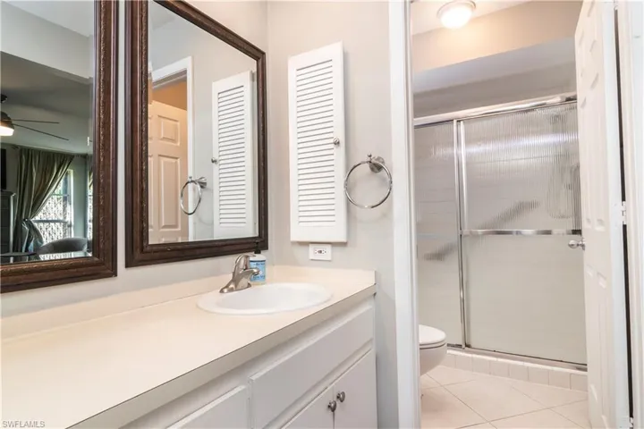 Bathroom with tile floors, a shower with shower door, vanity with extensive cabinet space, ceiling fan, and toilet