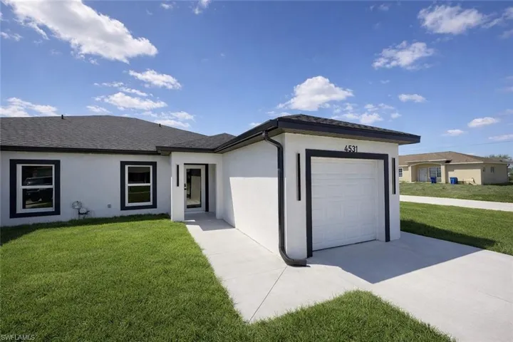 View of front of home with a front yard, a garage, concrete driveway, stucco siding, and a shingled roof