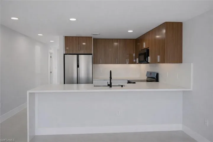 Kitchen with a peninsula, black appliances, backsplash, light stone counters, and recessed lighting