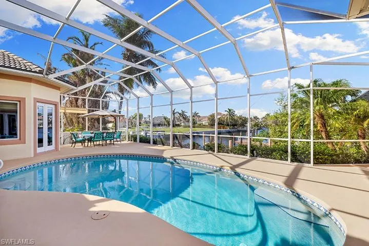 View of pool with glass enclosure, a patio area, and a water view