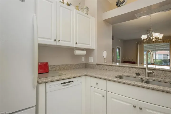 Kitchen with decorative light fixtures, white appliances, sink, and white cabinets