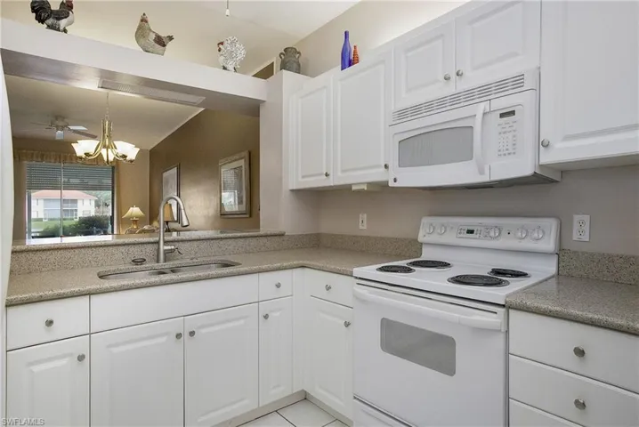 Kitchen with white cabinets, light tile patterned floors, white appliances, and sink