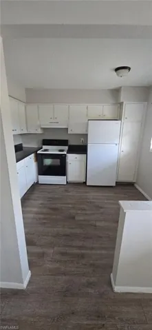 Kitchen featuring dark countertops, white appliances, dark wood-type flooring, white cabinets, and under cabinet range hood