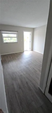 Empty room with a textured ceiling and dark wood-style flooring