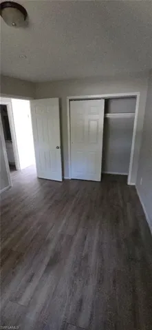Unfurnished bedroom with dark wood-style floors, a closet, and a textured ceiling