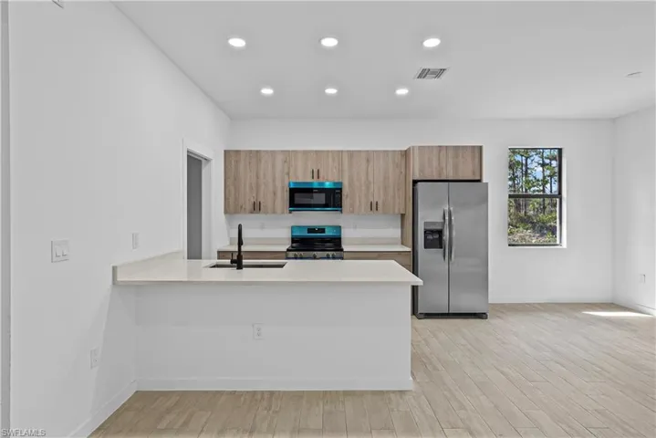 Kitchen featuring stainless steel appliances, a peninsula, light wood finished floors, recessed lighting, and light stone counters