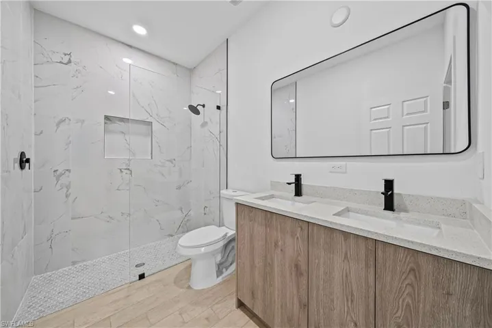 Bathroom with double vanity, a marble finish shower, light wood-type flooring, and recessed lighting