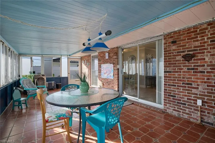 Enclosed patio featuring red brick walls, patterned tile flooring, a light blue paneled ceiling, and glass sliding doors