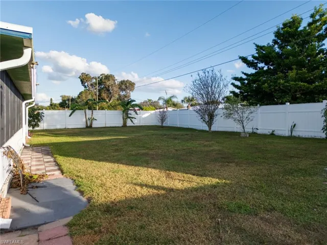 Expansive backyard featuring a green lawn, full white privacy fencing, and mature trees