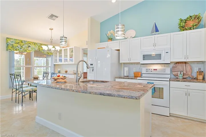 Kitchen with white cabinetry, an island with sink, pendant lighting, and white appliances