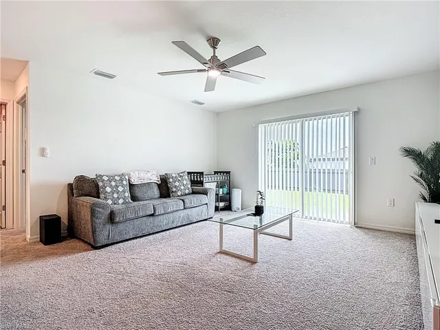 Carpeted living area featuring ceiling fan and baseboards