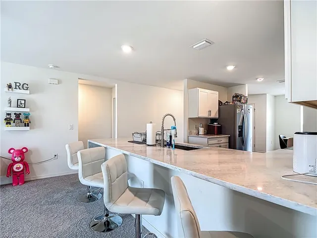 Kitchen featuring white cabinetry, light stone countertops, a breakfast bar area, stainless steel fridge with ice dispenser, and dark carpet