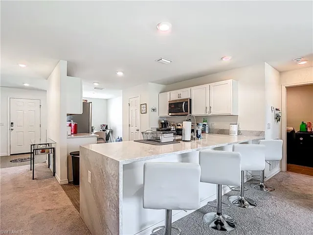 Kitchen featuring a peninsula, a kitchen breakfast bar, white cabinetry, dark carpet, and light stone counters