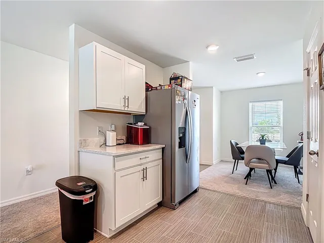 Kitchen with white cabinets, stainless steel fridge, light stone countertops, and light colored carpet