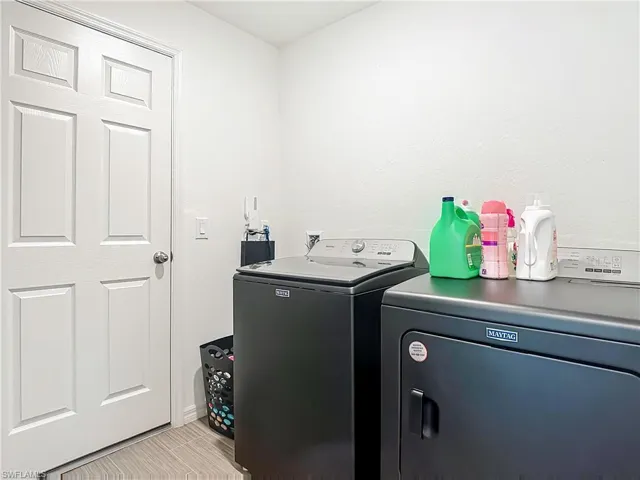 Laundry area with washer and clothes dryer and light tile patterned flooring
