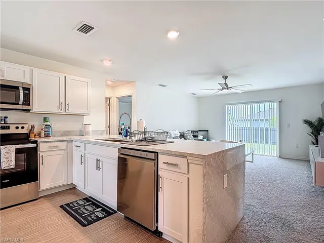 Kitchen with appliances with stainless steel finishes, light stone countertops, ceiling fan, and white cabinets