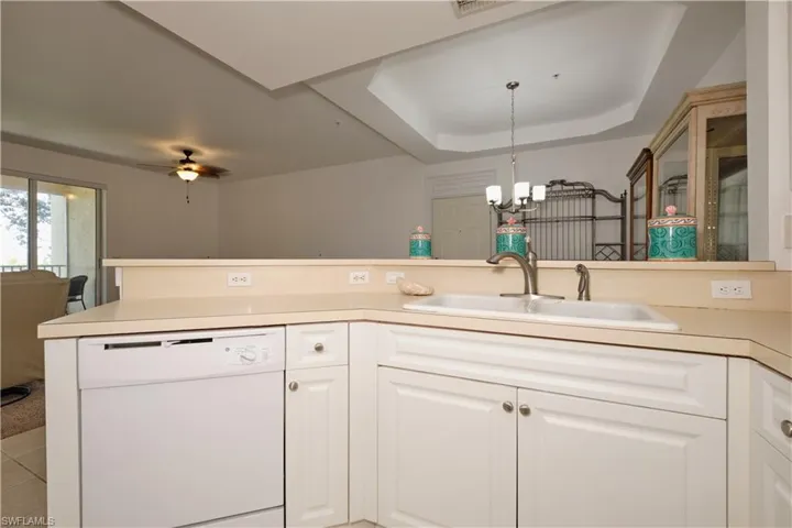 Kitchen with decorative light fixtures, ceiling fan with notable chandelier, dishwasher, a tray ceiling, and sink