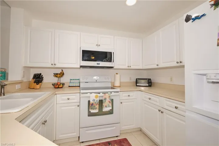 Kitchen featuring sink, white cabinetry, white appliances, and light tile floors