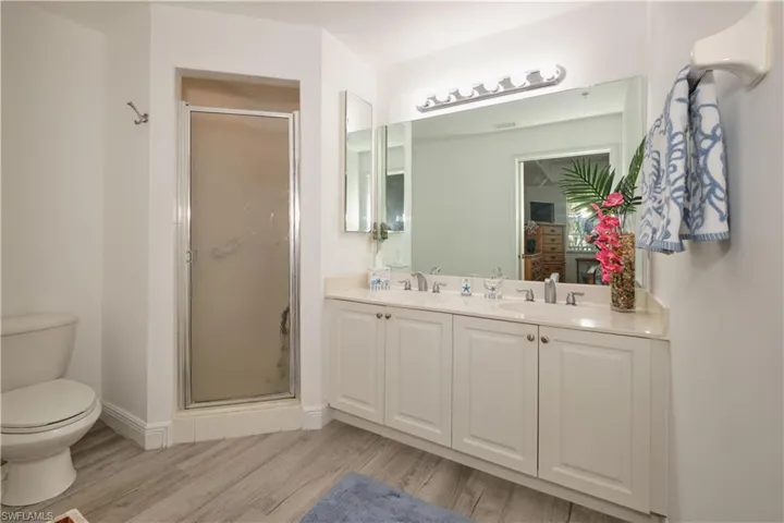 Bathroom featuring dual vanity, a shower with door, toilet, and wood-type flooring