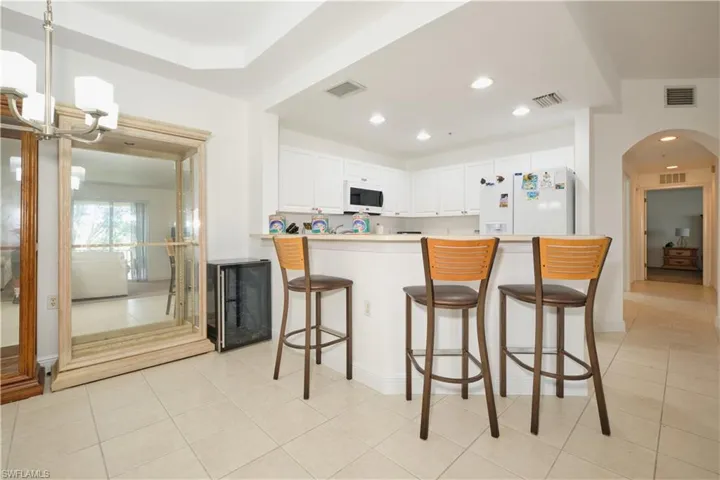 Kitchen with kitchen peninsula, a kitchen breakfast bar, white cabinetry, white appliances, and light tile floors