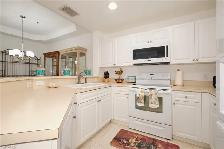 Kitchen featuring white cabinets, hanging light fixtures, sink, and white appliances