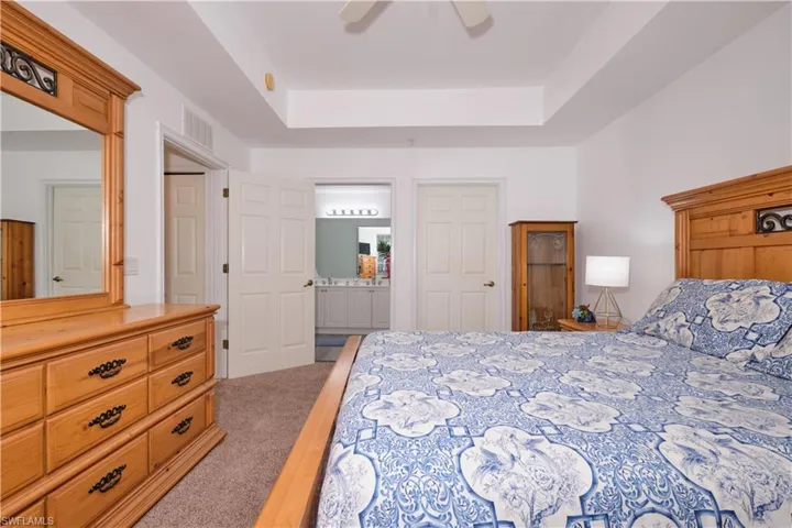 Bedroom featuring ceiling fan, a tray ceiling, ensuite bath, and carpet flooring