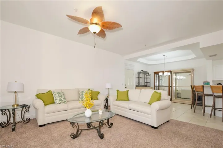 Carpeted living room featuring a raised ceiling and ceiling fan with notable chandelier