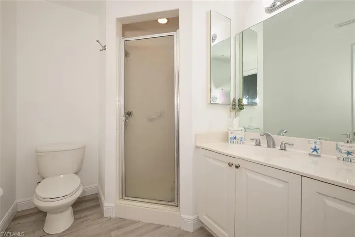 Bathroom with hardwood / wood-style floors, walk in shower, vanity, and toilet