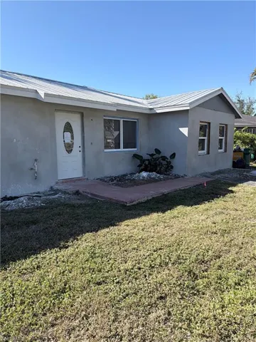 View of front of property with a front yard, stucco siding, and a metal roof