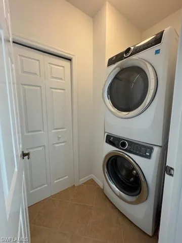 Laundry area featuring light tile patterned floors and stacked washing machine and dryer