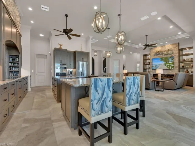 Open-concept kitchen featuring an oversized island with seating, integrated stainless steel appliances, granite countertops, and extensive custom cabinetry