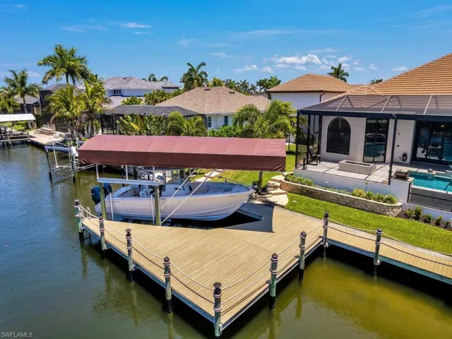 Waterfront property featuring a private boat dock with covered lift, a screened patio, outdoor swimming pool, and stone retaining walls