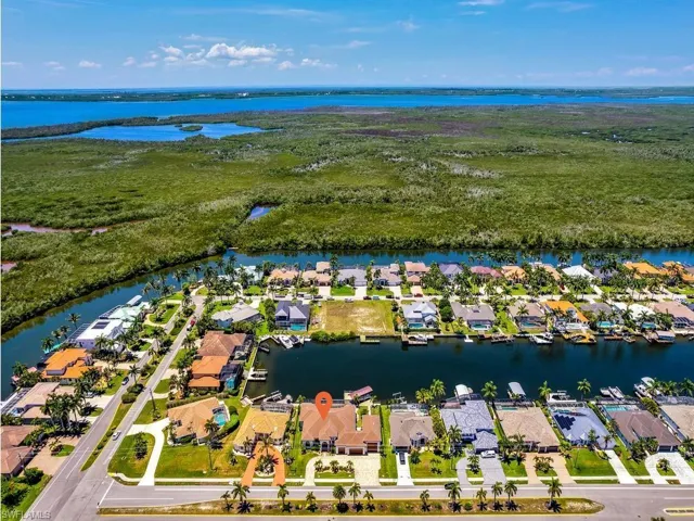 Aerial perspective showcasing a waterfront community with canal access, mature landscaping, and a distant body of water