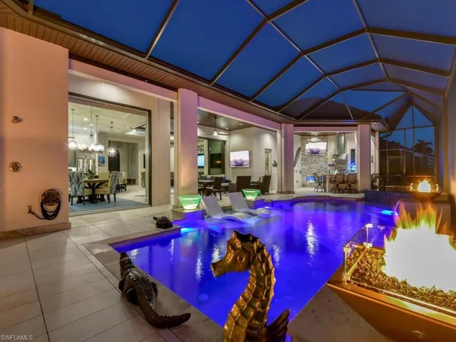 Screened pool enclosure featuring an illuminated pool with integrated spa and fire feature