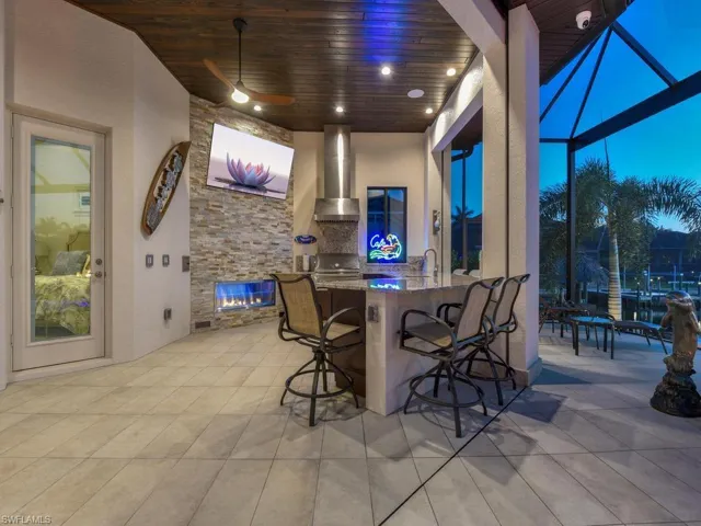 Outdoor kitchen featuring a stone-clad accent wall with a linear fireplace, integrated bar seating, and a wood-finish ceiling