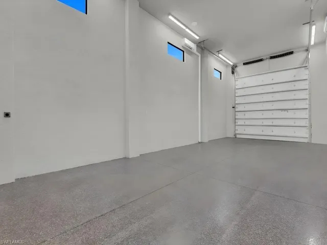 Spacious room featuring a concrete floor, high ceilings, multiple linear light fixtures, and transom windows