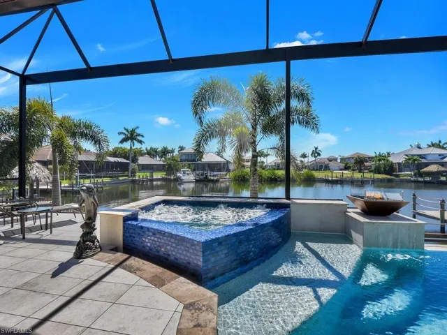 Screened outdoor living area featuring a built-in spa with blue tile surround, an integrated swimming pool, and a water-facing patio