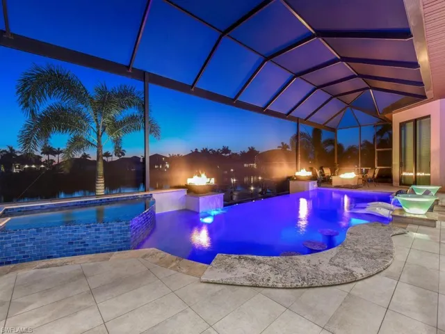 Screened patio enclosure featuring a swimming pool with integrated seating, an elevated spa with blue mosaic tile, and a surrounding paver deck