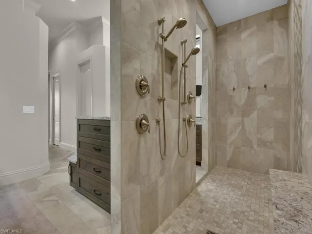 Spacious walk-in shower featuring large format tiled walls, dual shower heads with handheld sprayers, mosaic tiled floor, and a built-in stone bench
